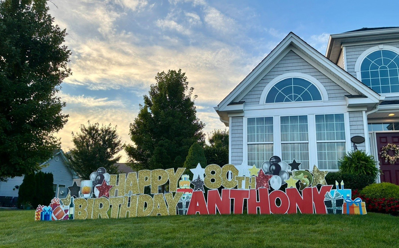 Happy 80th Birthday Anthony gold glitter yard card display with black and silver balloons, stars, and presents at sunset