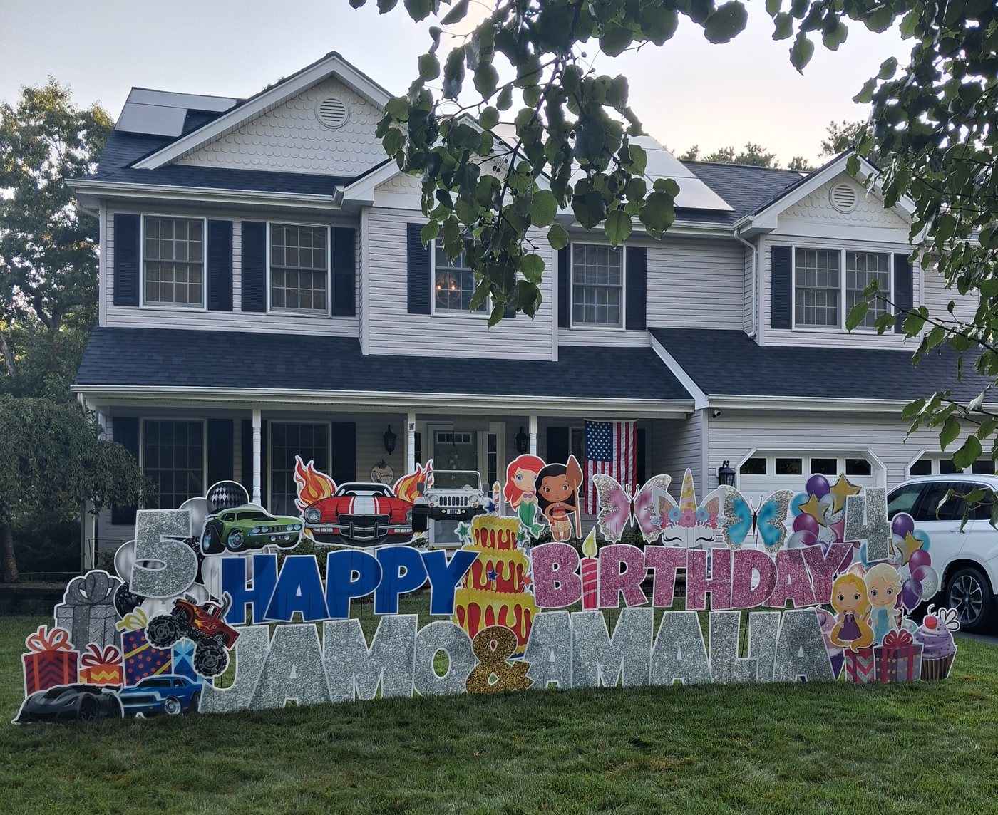Happy Birthday Jamo and Amalia sibling yard card display with monster trucks, race cars, princesses, and unicorns